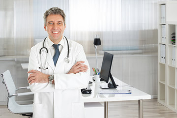 Confident Male Doctor Standing Arms Crossed In Clinic