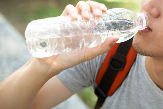 Close up of man drinking mineral water from bottle in the park - health care concept