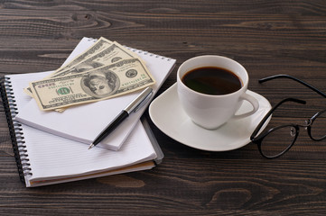 On wooden office desk, stack notepads, pen, coffee and money