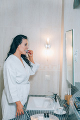 Portrait of attractive woman brushing teeth in bathroom  a white coat. healthy teeth.