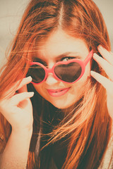 Holidays, vacation travel and freedom concept. Beautiful redhaired happy girl in heart shaped sunglasses on beach.