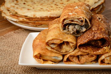 Crepes stuffed with chicken and mushrooms on wooden table.