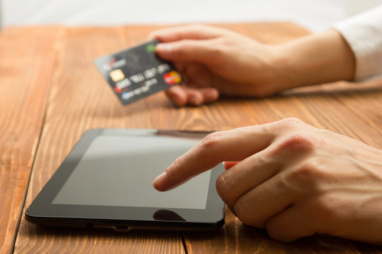 Hands holding credit card typing numbers on tablet pc making online payment at home the wooden table. Online shopping concept. Selective focus.