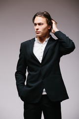 Charming handsome. Full length of handsome young man in full suit and bow tie adjusting his sleeve while standing against grey background