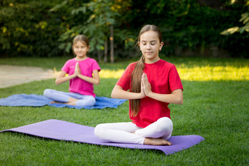 Two smiling sisters practicing yoga on grass at park