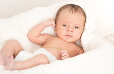 Smiling baby boy lying on soft beige blanket and cushion