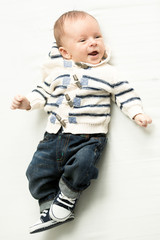 smiling baby boy in jeans and sweater lying on bed