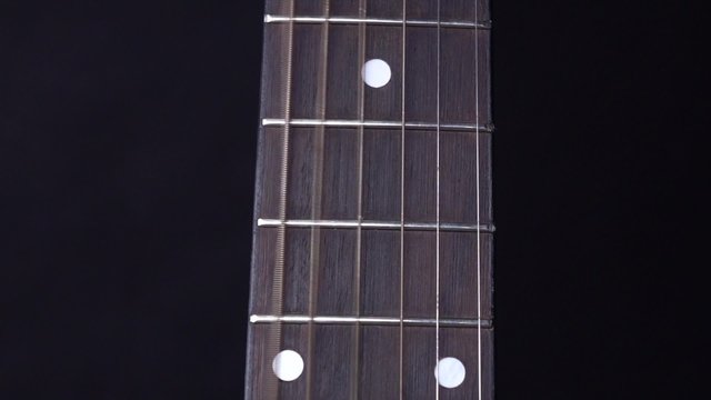 Playing string of acoustic guitar, stands up, on black, close up, slow motion