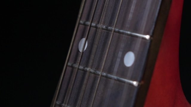 Play strings of acoustic guitar, side view, on black, close up, slow motion