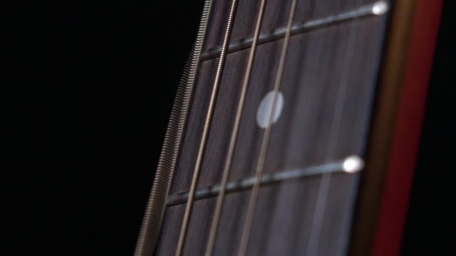 Playing strings of acoustic guitar, down view, first string, on black, close up, slow motion