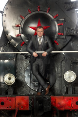 Retro styled businessman in suit posing on steam locomotive