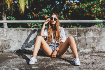 young beautiful girl hippies in sunglasses poses next to an abandoned house