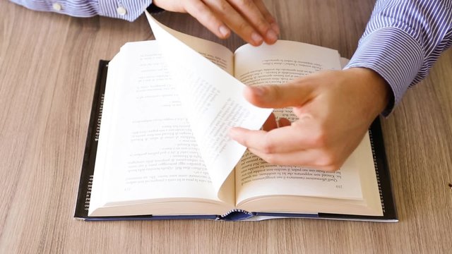 mani che sfogliano pagine di un libro mentre si legge su un tavolo