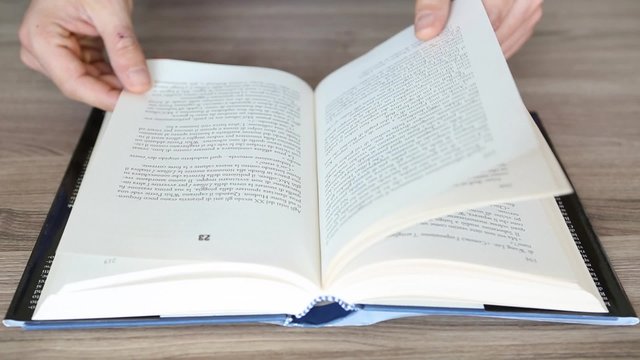 mani che sfogliano pagine di un libro in lettura su un tavolo di una biblioteca