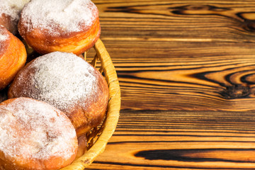 Homemade fresh donuts sprinkled with powdered sugar in wicker basket on wooden table, space for text