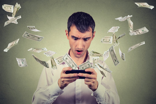 Shocked young man using smartphone with dollar bills banknotes flying away