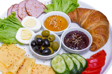 Plate of breakfast with croissant, boiled egg, meat and cheese