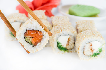 close up of chopsticks taking portion of sushi roll on the table