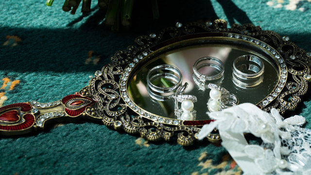 Wedding rings and earrings lying on a mirror. Wedding accessories