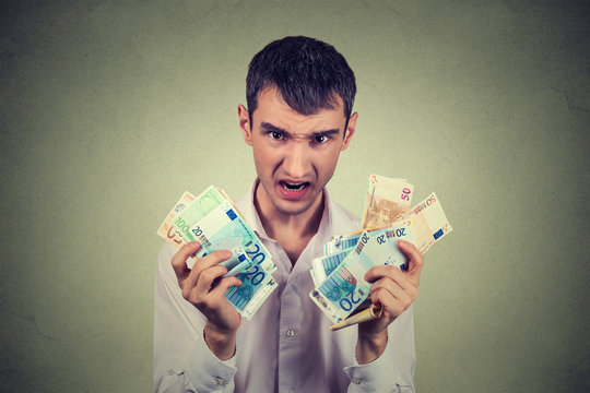 Greedy man with euro banknotes bills isolated on gray wall background