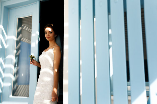 Elegant brunette bride in white dress posing near doorway with b