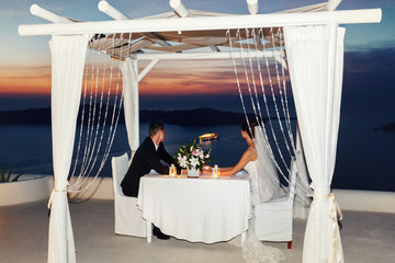 Bride and groom at sunset sitting at white table in tent sky bac