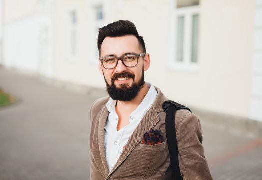 Outdoor street portrait of young fashion handsome hipster man with vintage glasses and camera,relaxing after work,weather jacket and mens accessorizes ,Hipster bearded man 

