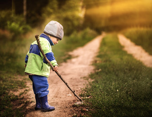 Boy playing outdoor with wooden stick on country rural road.