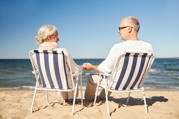 happy senior couple in chairs on summer beach - Powered by Adobe