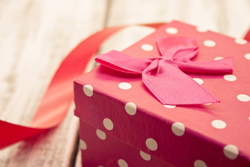 Red gift box with ribbon on rustic white wooden table. 