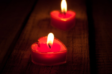 Red burning heart shaped candles on rustic wooden table. 