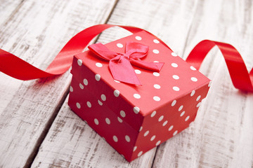 Red gift box with ribbon on rustic white wooden table. 
