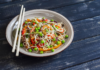 Rice noodles with vegetable stir fry on the ceramic plate on dark wooden background