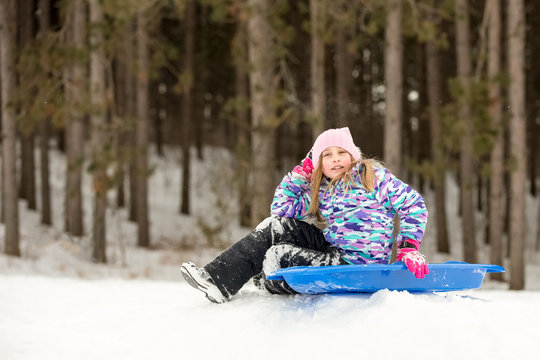 Confident Girl Sitting with Her Sled on a Hill