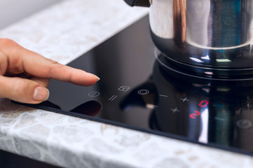 Woman hand turns on modern induction kitchen