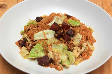 Fried instant noodle with chinese sausage and vegetable on white dish on clean wood background