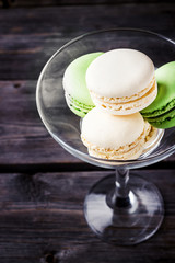 Macaroons in a glass on a high leg. Dark wooden background, selective focus.