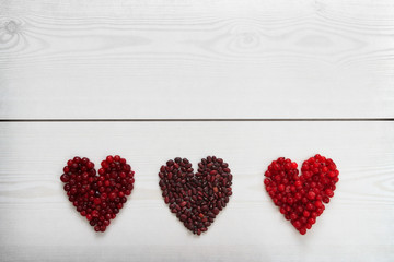 Red current, cranberries and beans in heart shape on wooden board