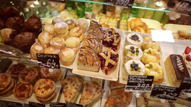 Shop window in a bakery or grocery shop with wide choice or range of various deserts. Tarts, pies, creamy cakes, chocolate sweets, pancakes with stuffing.