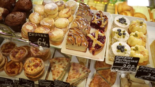 Shop window in a bakery or grocery shop with wide choice or range of various deserts. Tarts, pies, creamy cakes, chocolate sweets, pancakes with stuffing.