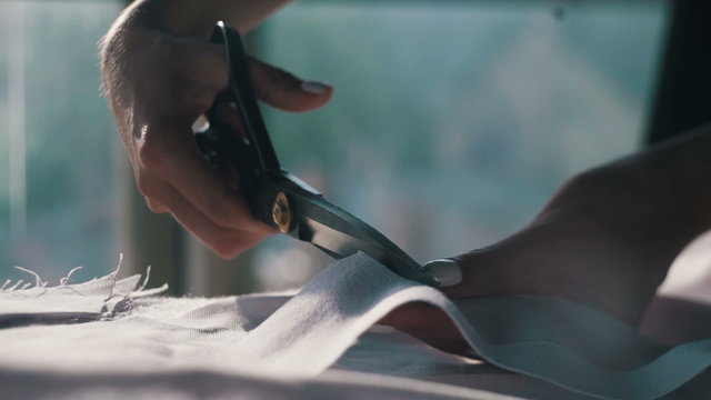Designer cuts cloth with scissor, close up, tilt shift