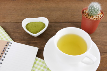 The cup of Japanese green tea and small note book with green cotton fabric on wooden planks.