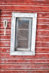 Crooked wood framed window in a faded red wall of painted boards