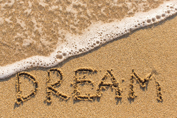 Dream - inscription on sand beach with the soft wave.