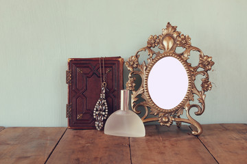 Antique blank Victorian style frame and old book with vintage necklace on wooden table. retro filtered image. template, ready to put photography
