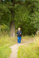 Fototapeta premium An elderly woman on a walk in the Park practicing Nordic walking.