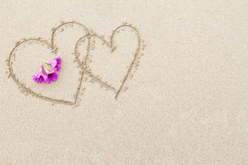 Fototapeta na wymiar Two hearts with pink flowers on the beach surface background