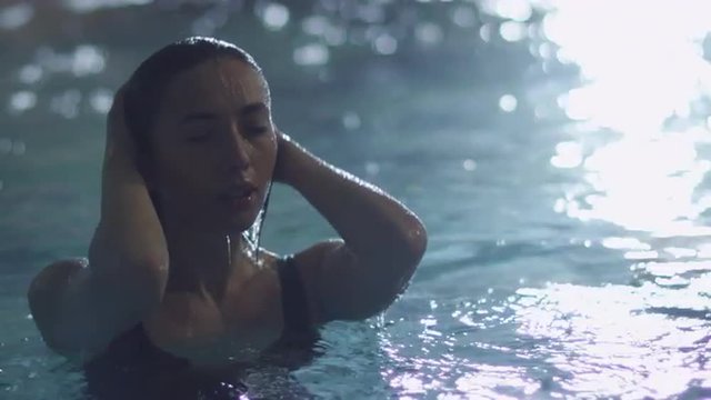 Young attractive female dives out of the water in a pool in a spa wellness center. Shot on RED Cinema Camera.