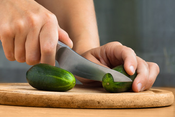 hands slicing cucumber on wooden cutting board