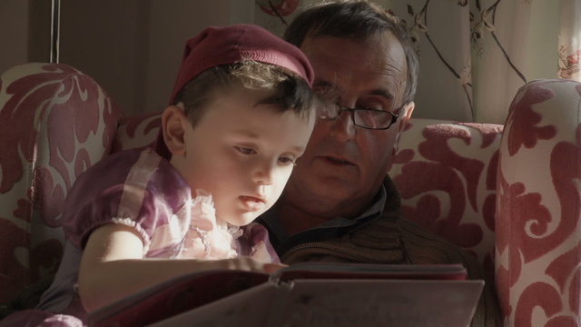 A granddad is reading a story book to his  grandson. The grandson is dressed up as a princess from the story in the gender blender style. Shot in super slow motion at 240fps